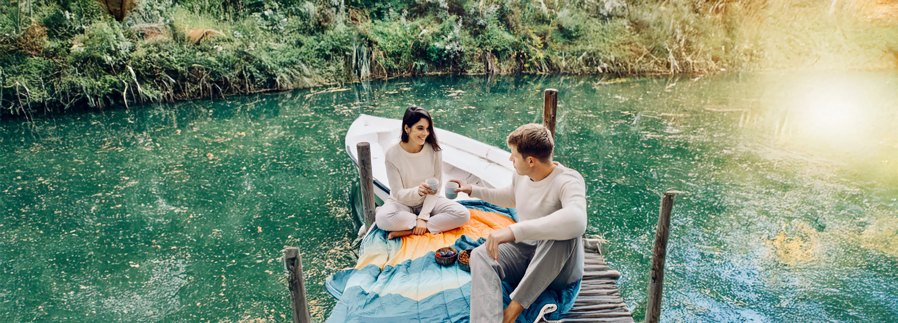 Ein Paar genießt ein Picknick auf einem Bootssteg – auf einer gemütlichen Outdoor-Decke mit liebevoll angerichteten Snacks.
